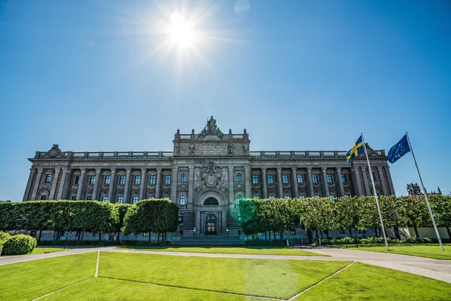 Front view of the Riksdag building with Swedish and EU flags on a sunny day. Från första avtal till återkommande intäkter