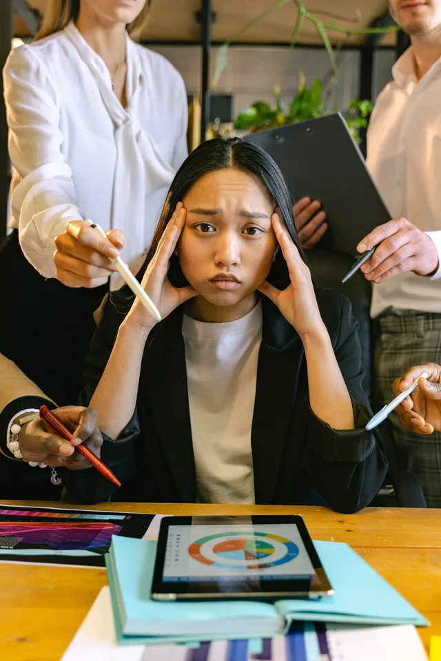 A stressed young woman overwhelmed with work at the office, surrounded by colleagues and devices. Processkartläggning för växande bolag