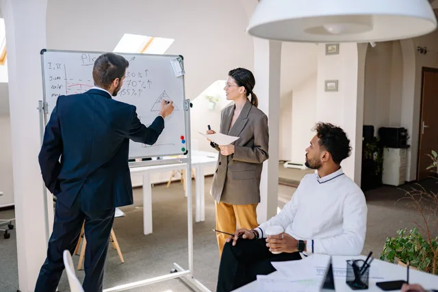 Diverse colleagues collaborating on a project using a whiteboard in a modern office setting. Rekrytering i snabbväxande bolag: från behov till onboarding